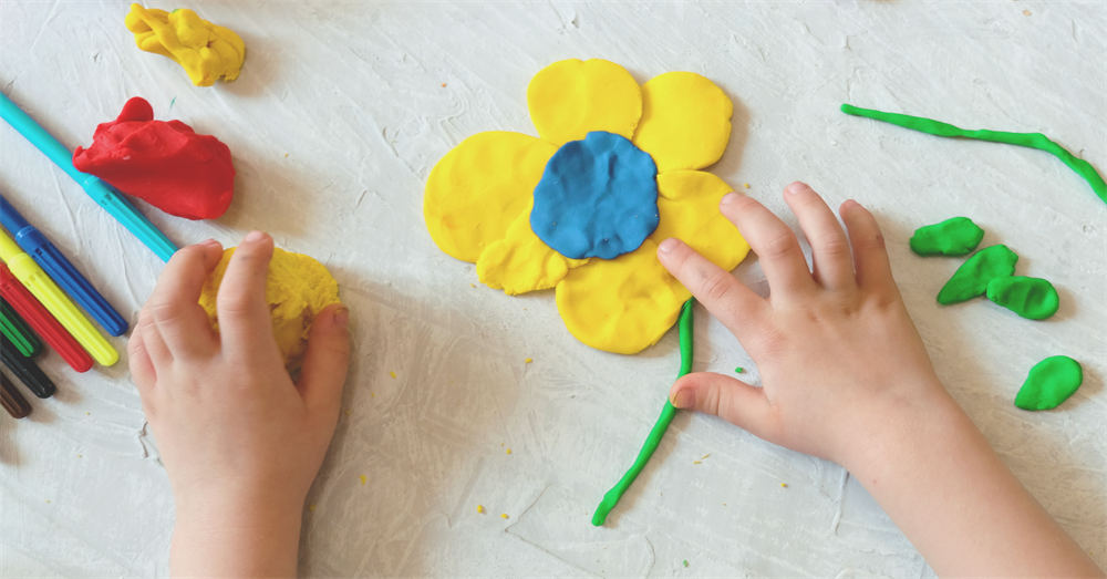 Hands of little girl making flower and sun and other from colorful clay dough, plasticine