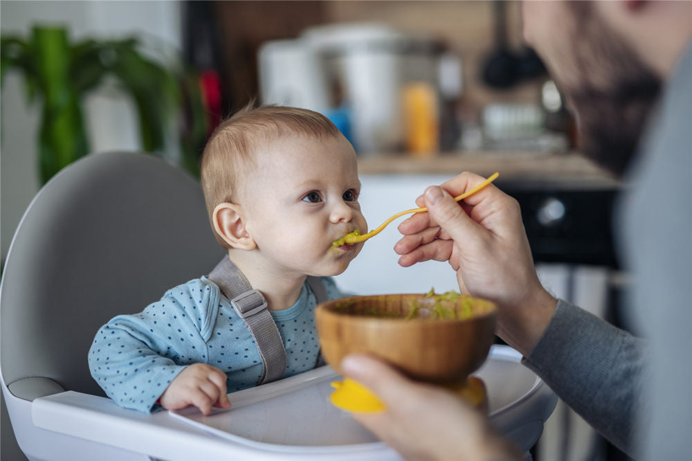 Caring single father spoon feeding his beautiful son at home