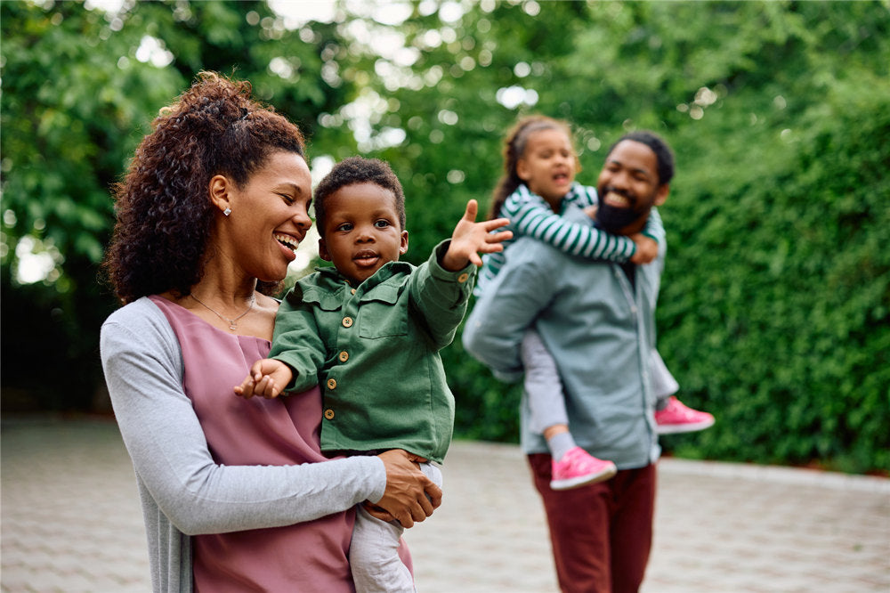 Happy African American woman holding her small son while walking outdoors. Father and daughter are in the background