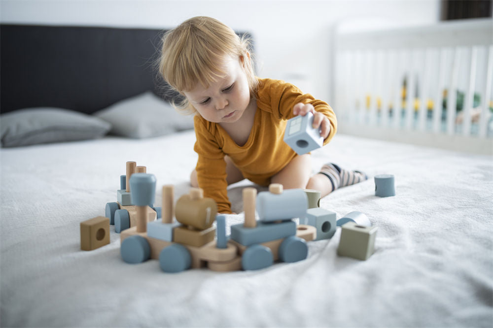 Happy little boy at home playing with wooden blocks and making a toy train