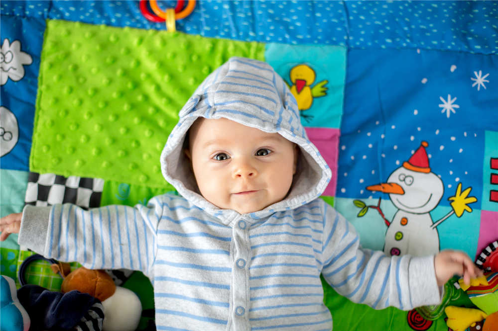 Happy three months old baby boy, playing at home on a colorful activity blanket