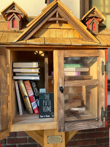 Image of a Little Free Library shaped like a wooden house with its door open and filled with books