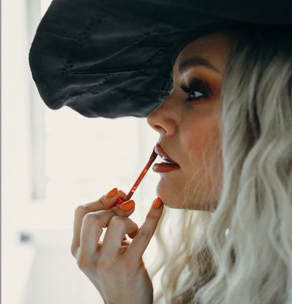 Woman with orange heroine.nyc nail polish applying orange lipstick for Halloween