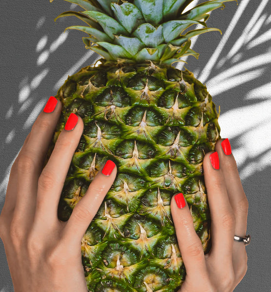 Hands with bright heroine.nyc nail polish holding an ananas