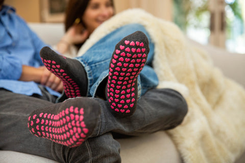 couple wears matching non-slipp grip socks to relax on couch under cozy fur blanket
