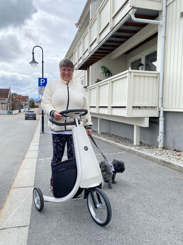 Kvinne med hund står bak en lys Movu i Kongsberg sentrum