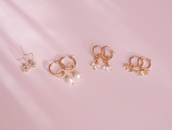 A collection of gold-filled earrings on a pink background