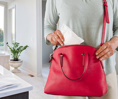 A person packs incontinence products into a purse before leaving the house.