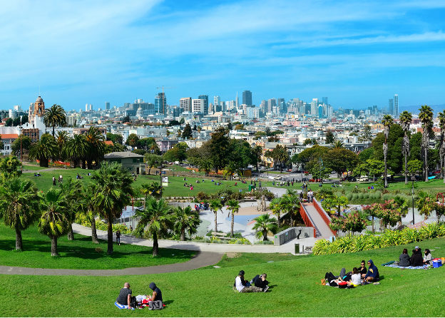 A lush green lawn of revelers relaxing with a view onto the blue skies and busy city of San Francisco