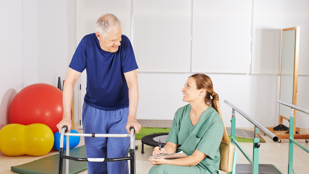 A man stands with a walker smiling at a healthcare professional.