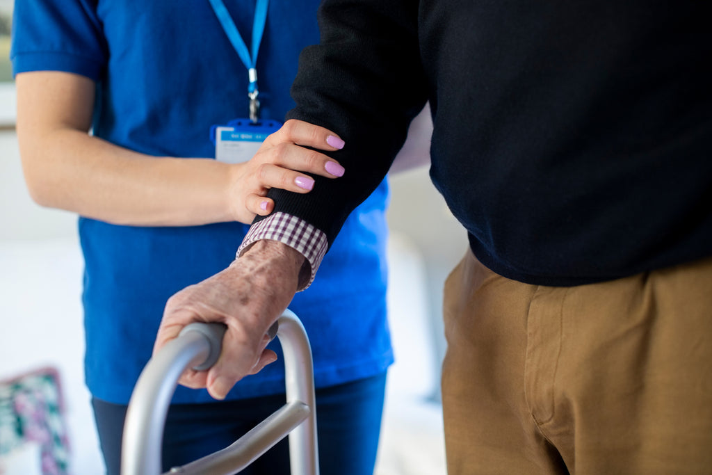 A medical staff member places their arm on a person while they hold onto a walker handle.