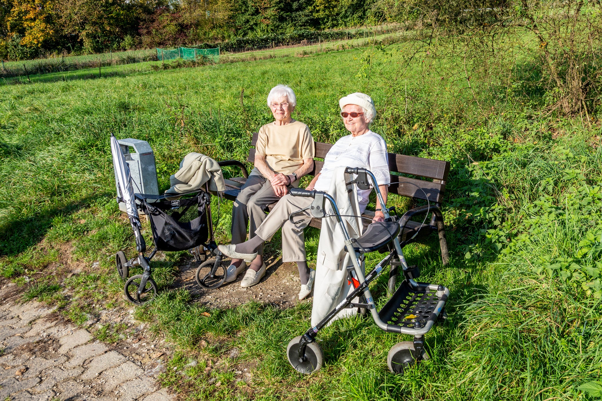 Two women with rollators on an uneven brick path.