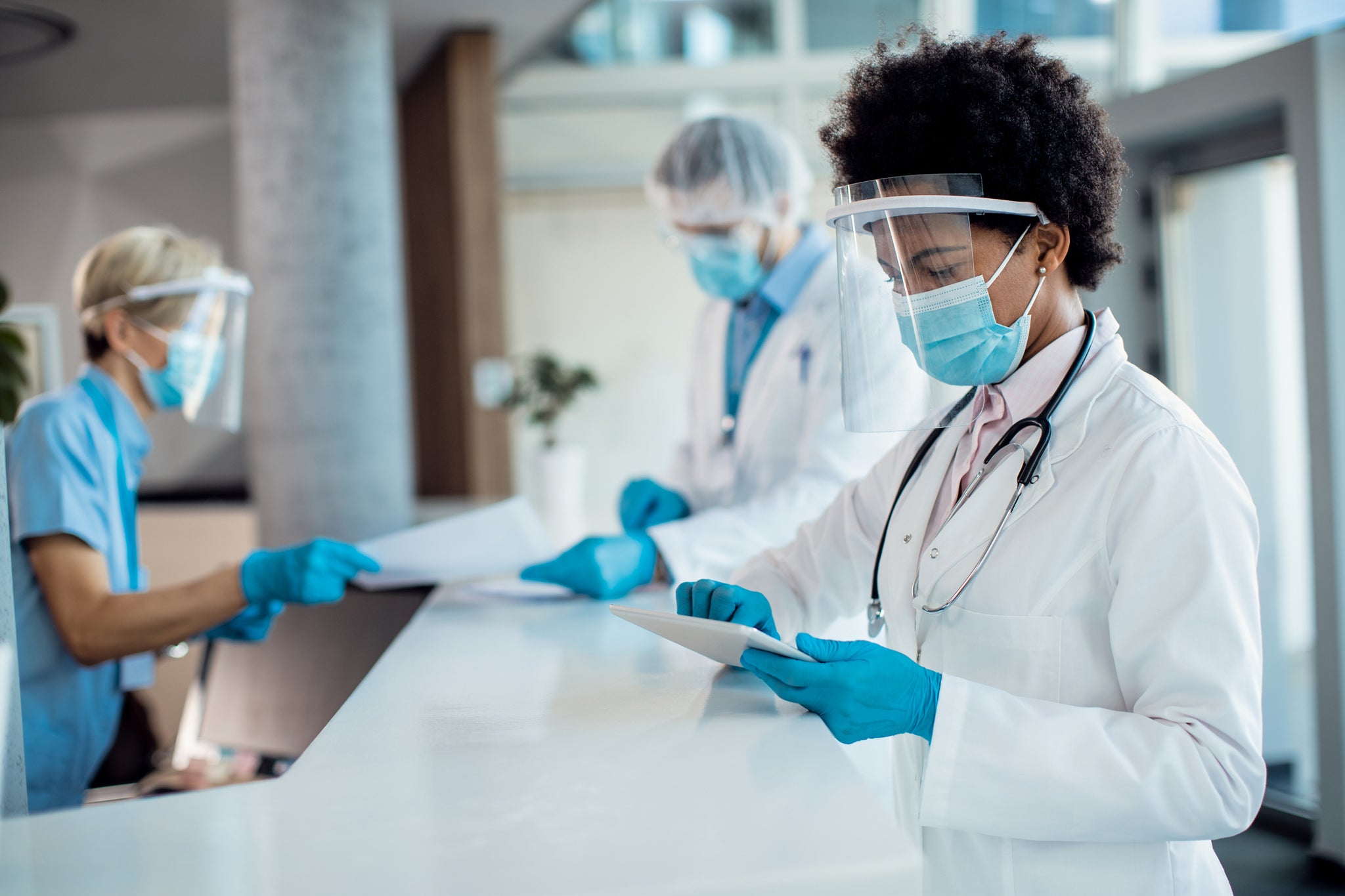 A doctor wearing a face shield and a mask reviews a chart.