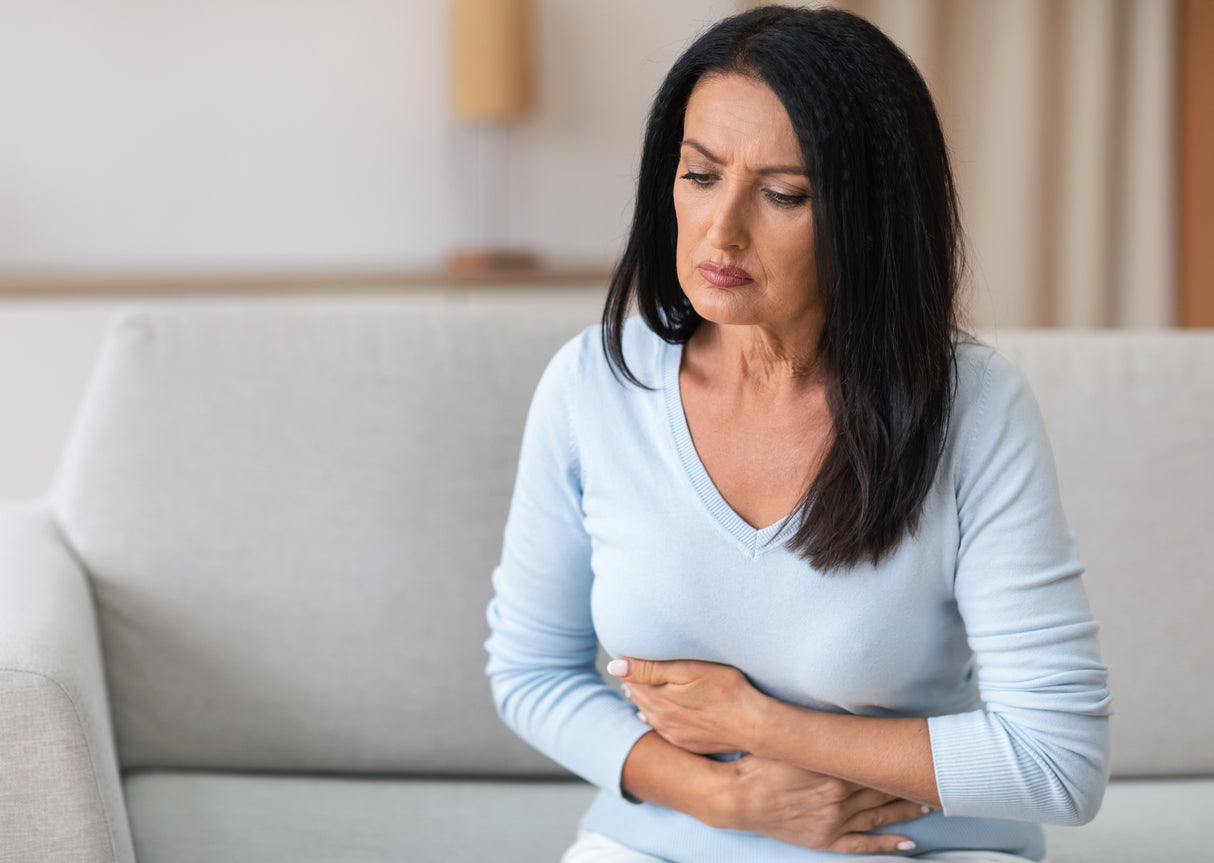 A woman sits on a couch holding her stomach in discomfort.