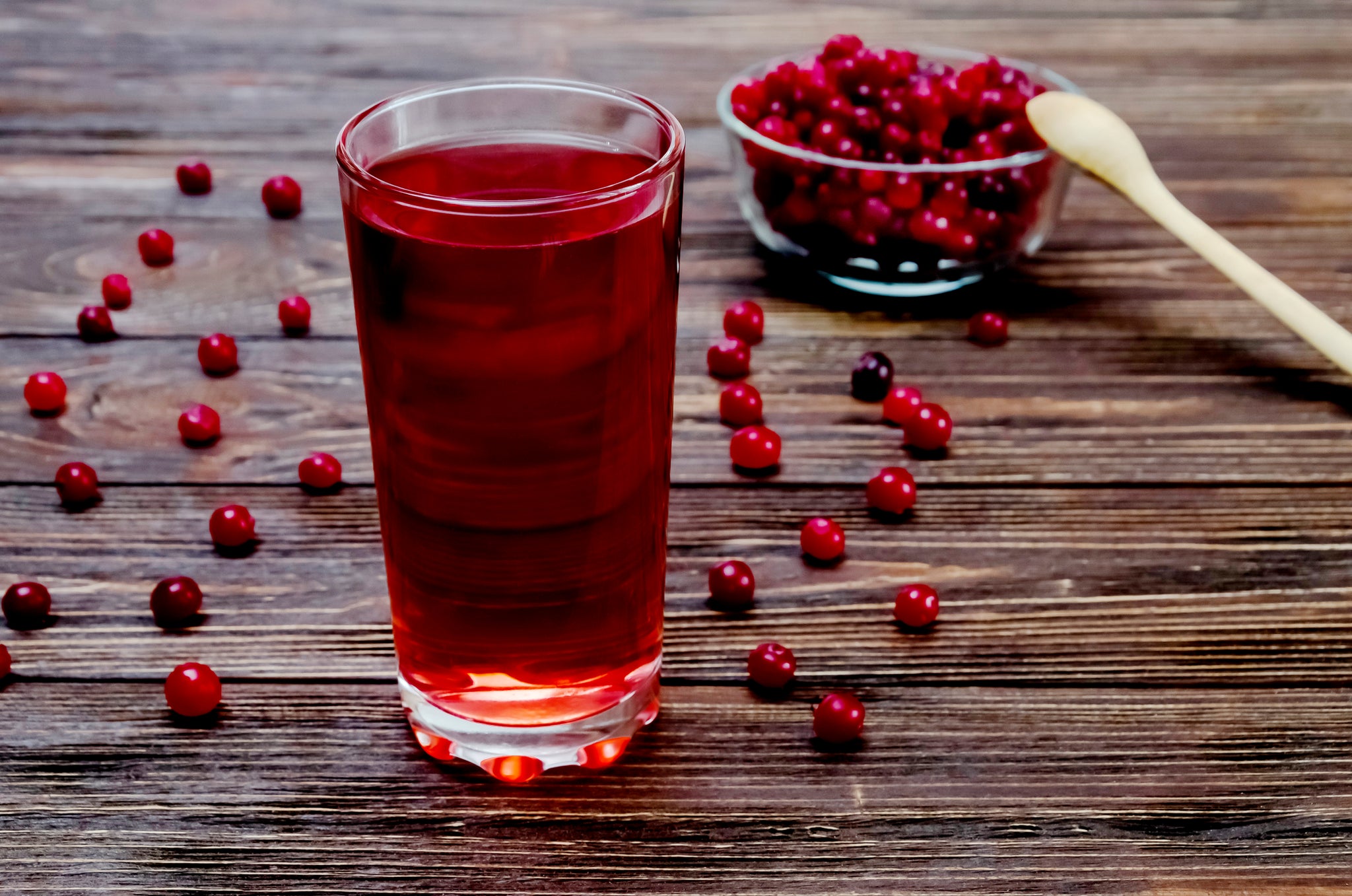 Cranberry and drink in glass glass on brown wooden background