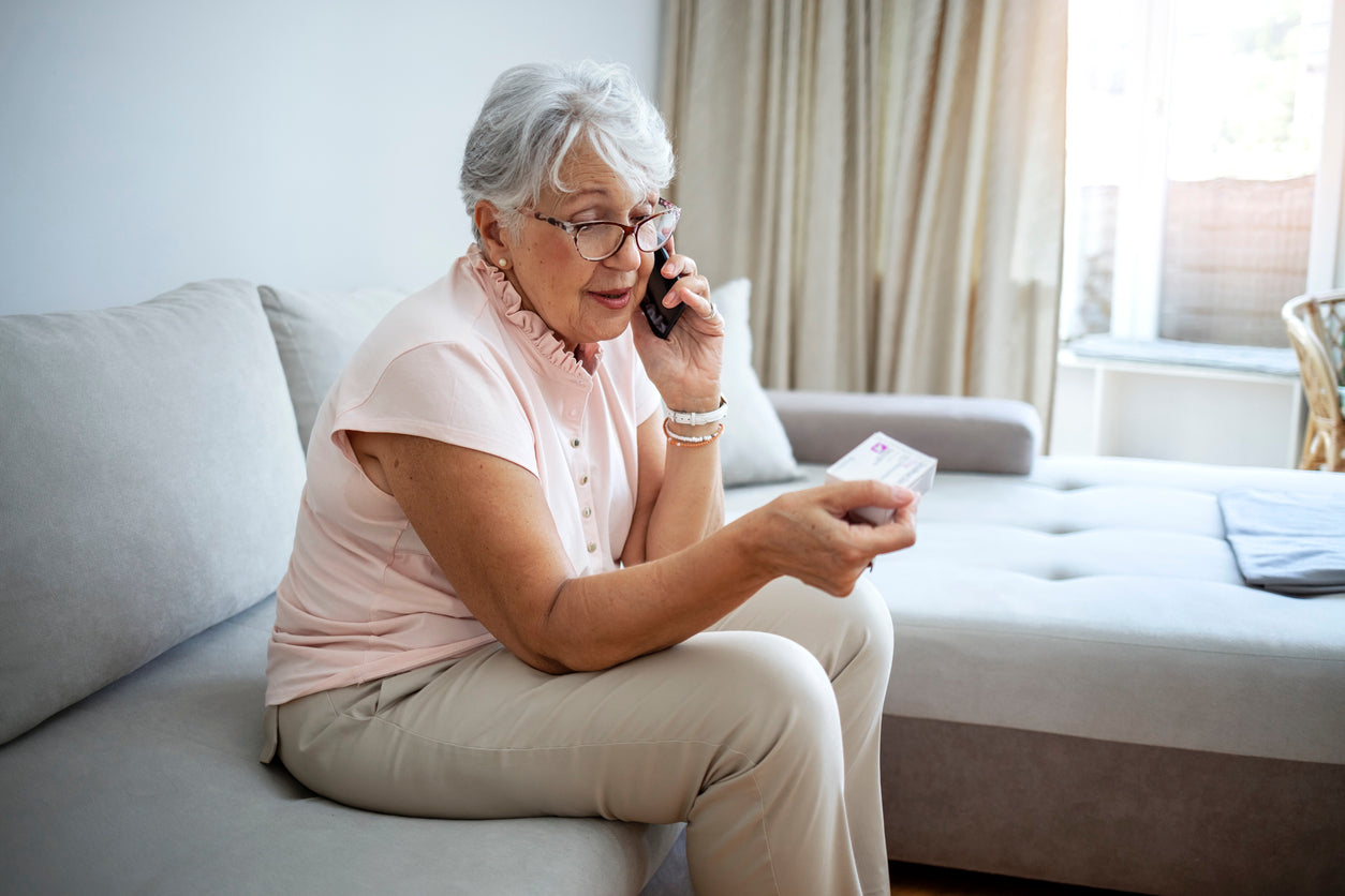 A woman speaks on the phone while looking at a medication box.