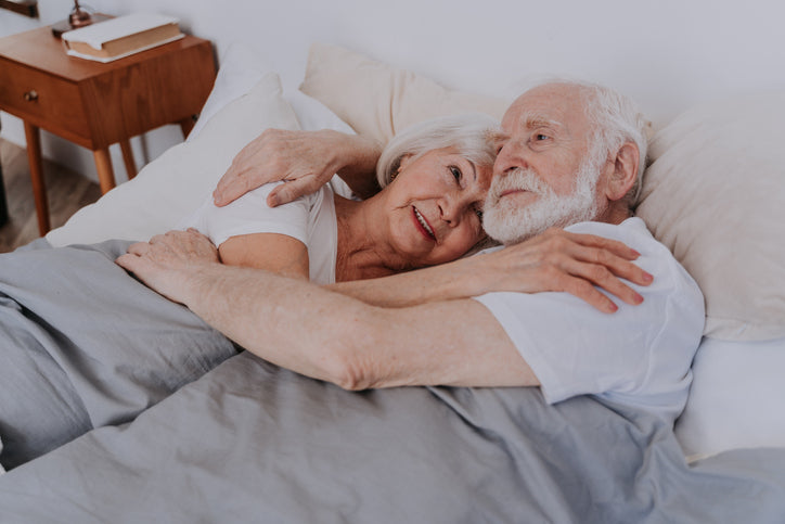 A couple lays in bed together cuddling.