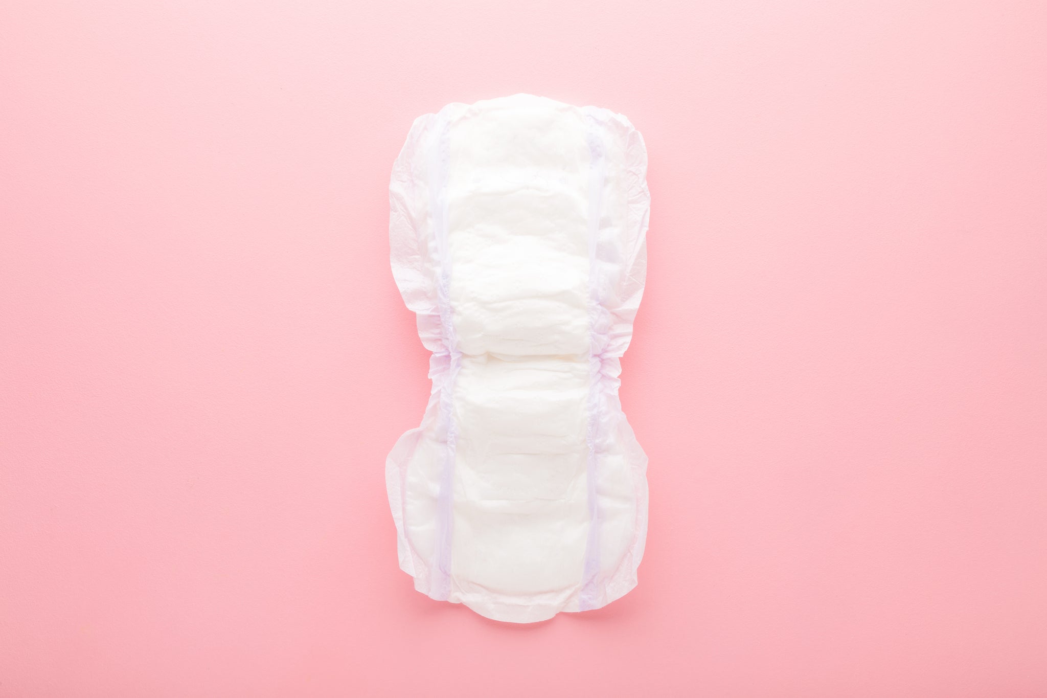 Opened white big size sanitary towel on pink table background. Pastel color. Closeup. Hygiene product for urinary incontinence or after childbirth. Top down view.