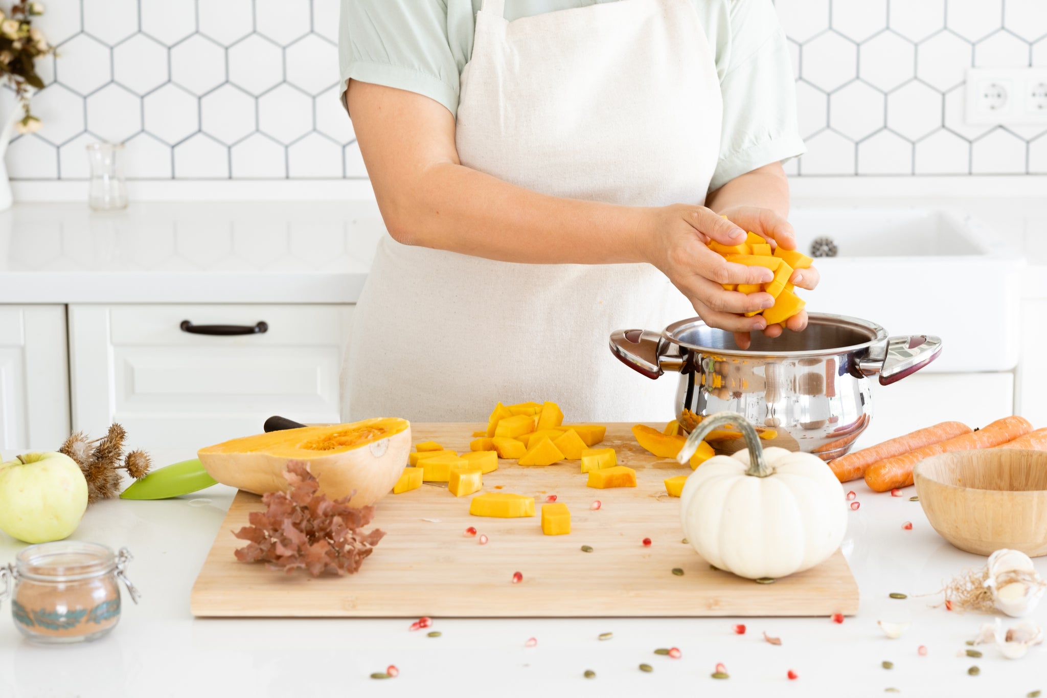 Woman hands putting a butternut pumpkin into a saucepan in modern white kitchen. Making pumpkin soup at home. Autumn recipe. High quality photo