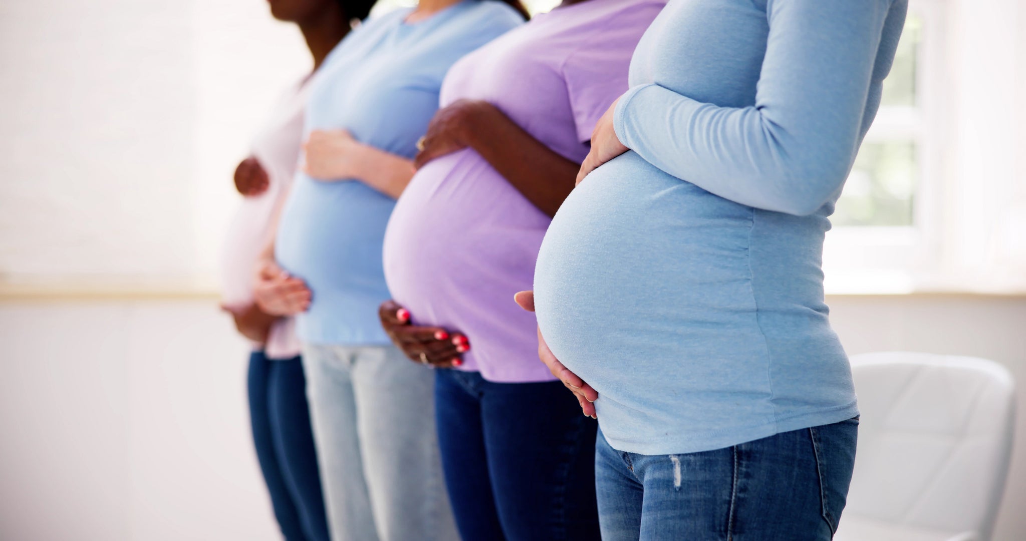 Four pregnant women stand in a line holding their stomachs.