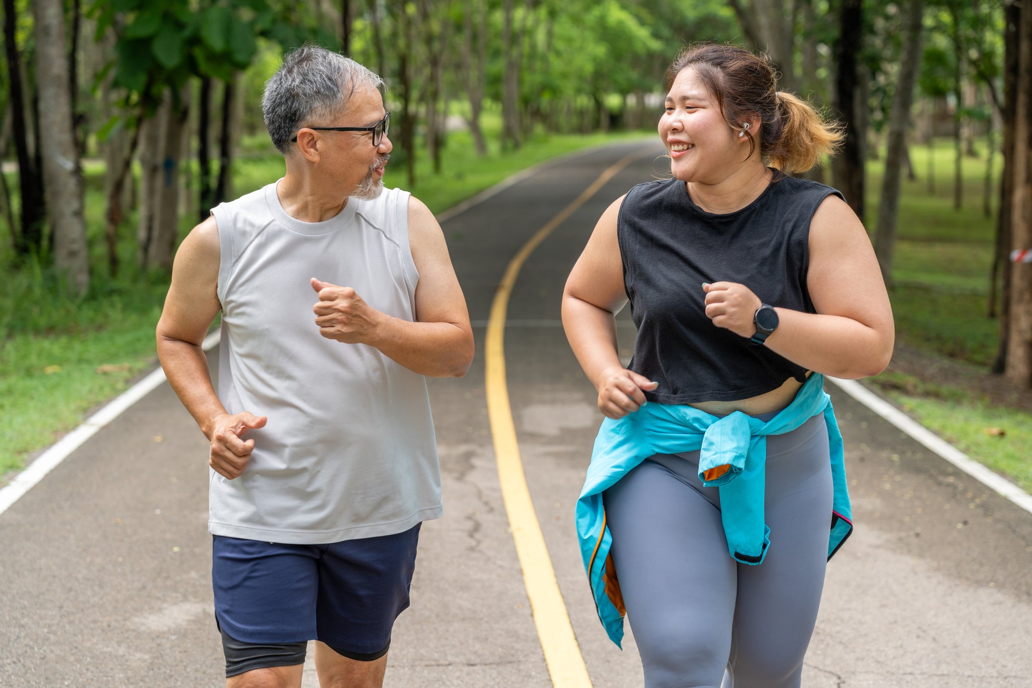 Two people run on a tree lined road.