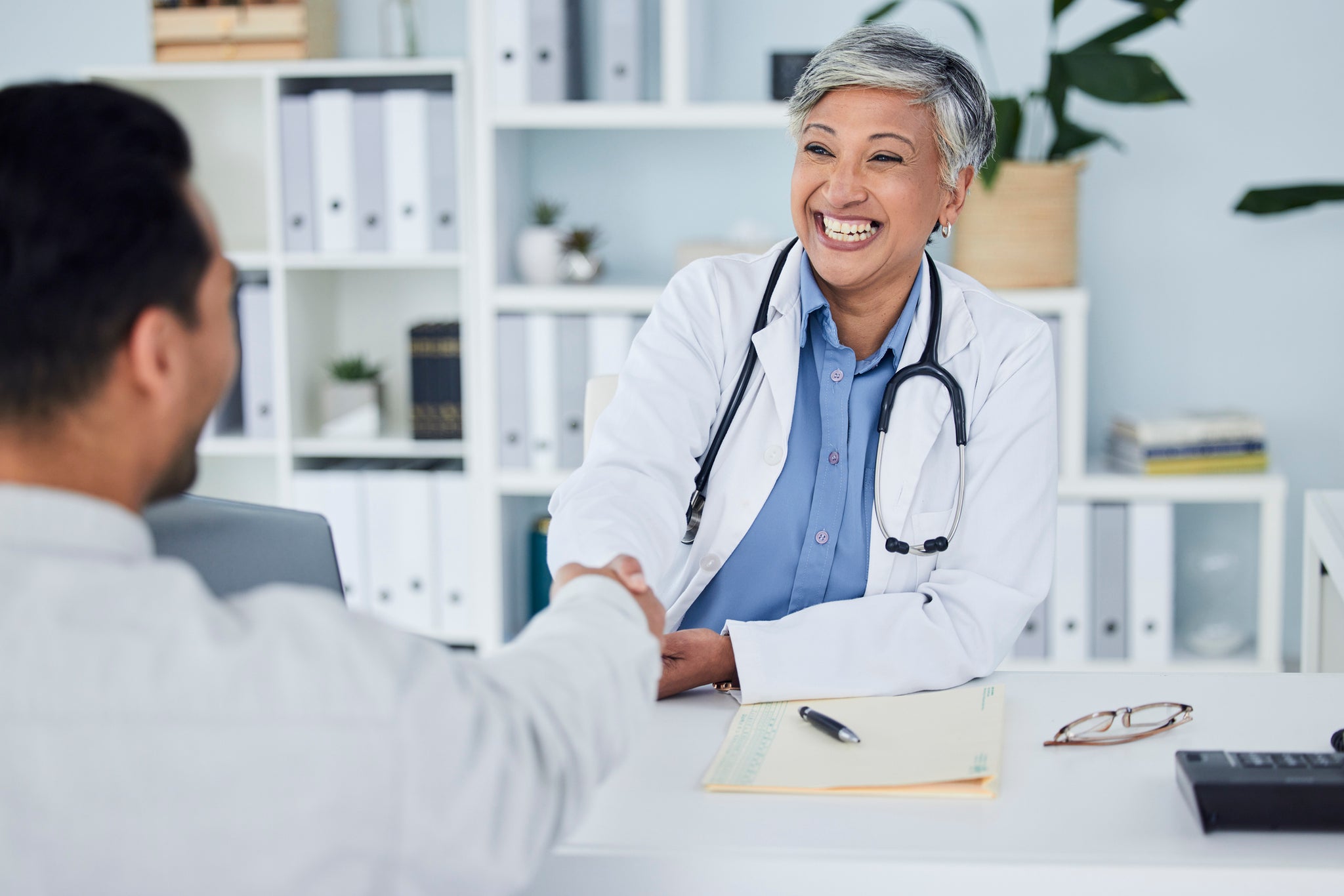 A doctor shakes hands with a patient in an office.