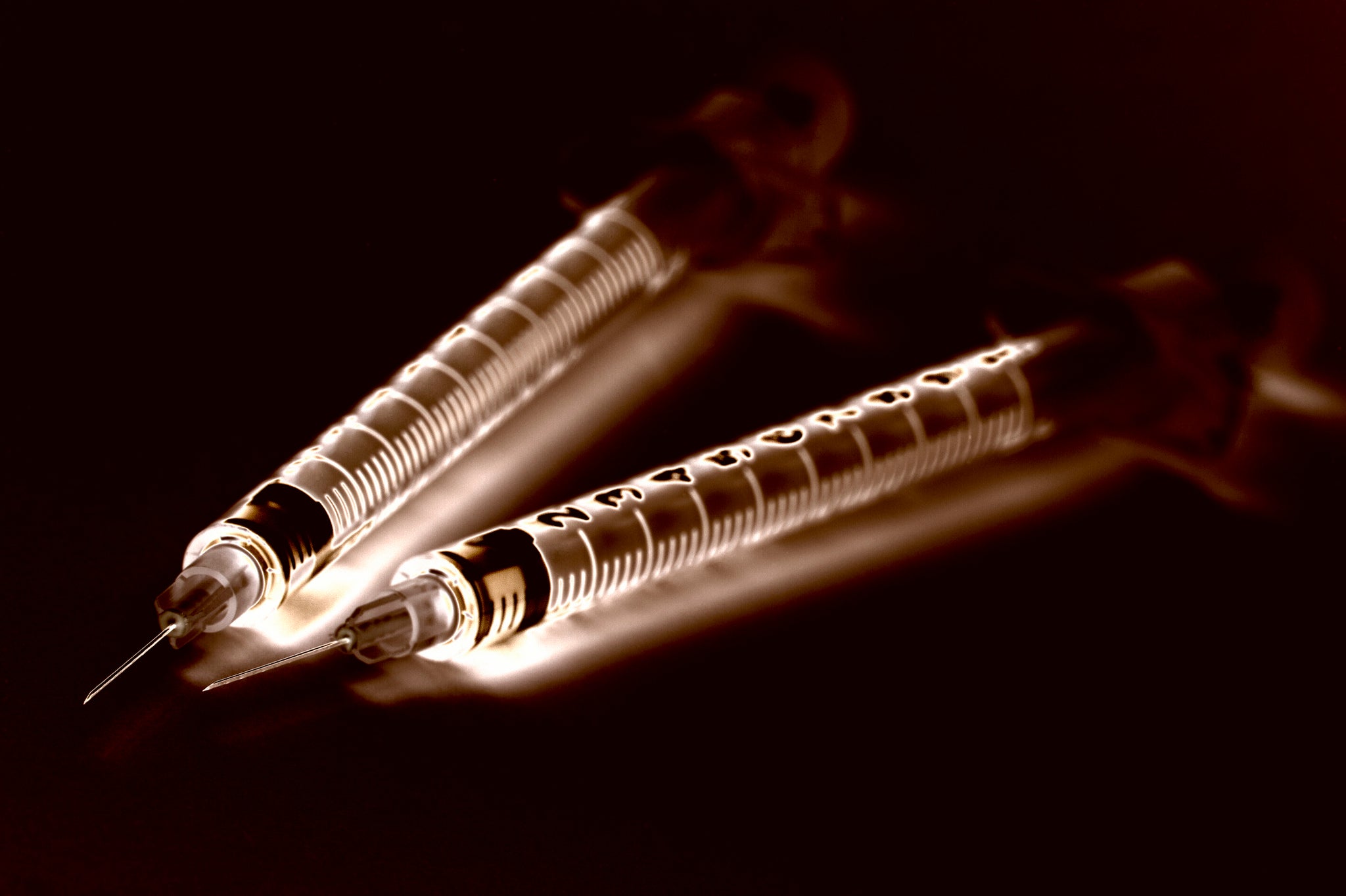 Two syringes lit against black.