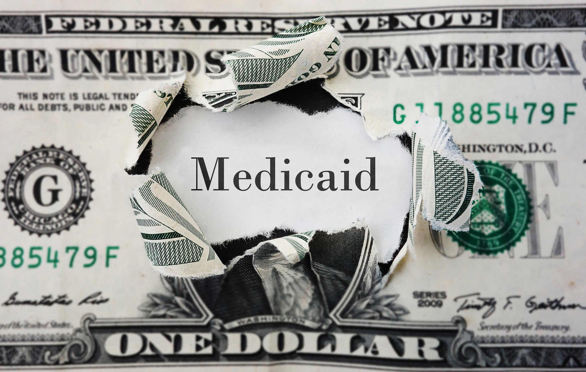 A US dollar ripped to reveal the word "Medicaid".