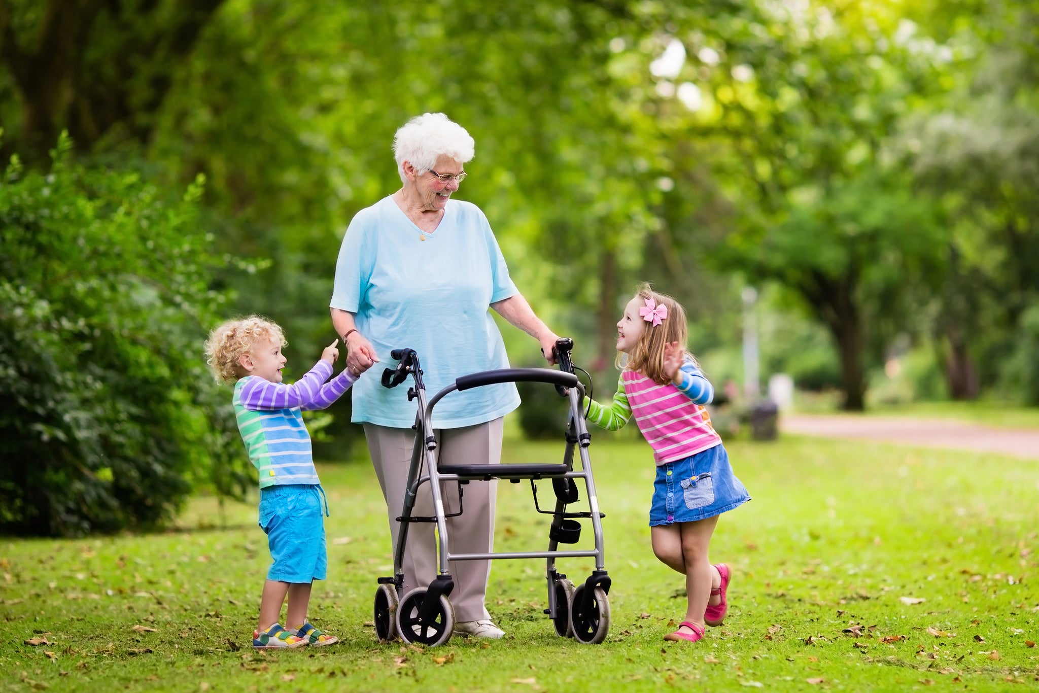 A grandmother using a rollator in a park with two grandchildren.