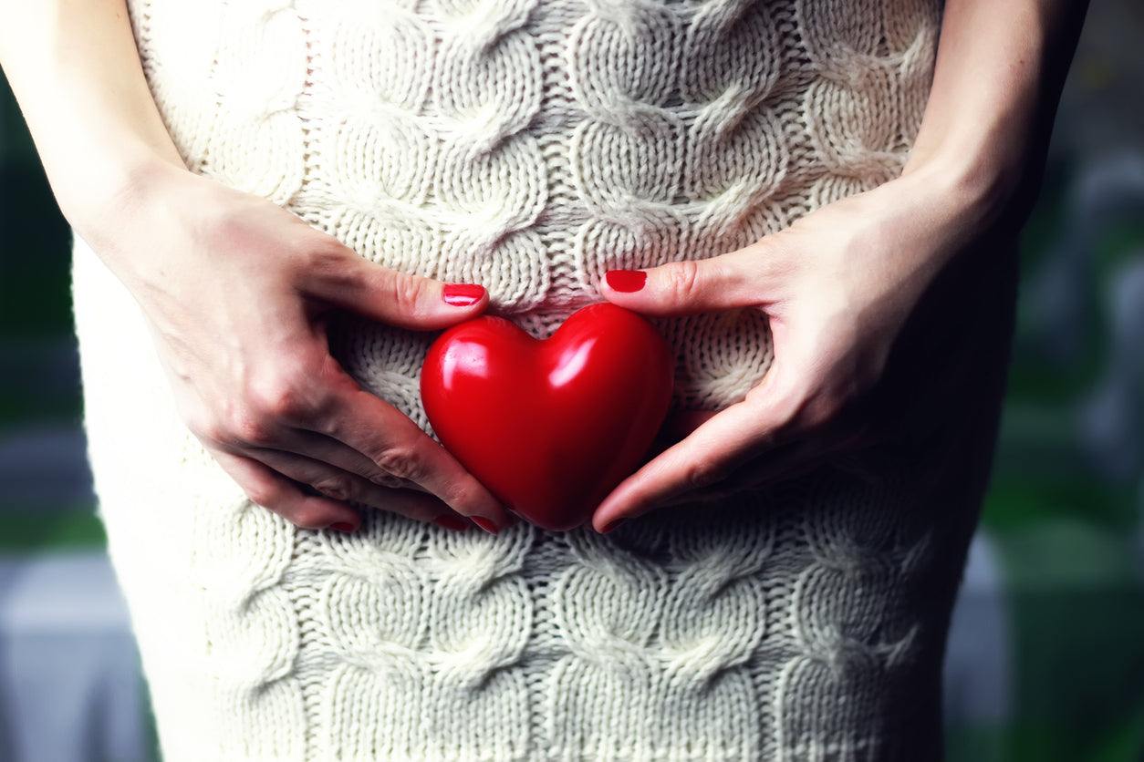 A woman in a knit dress holds a heart over her pelvic region.