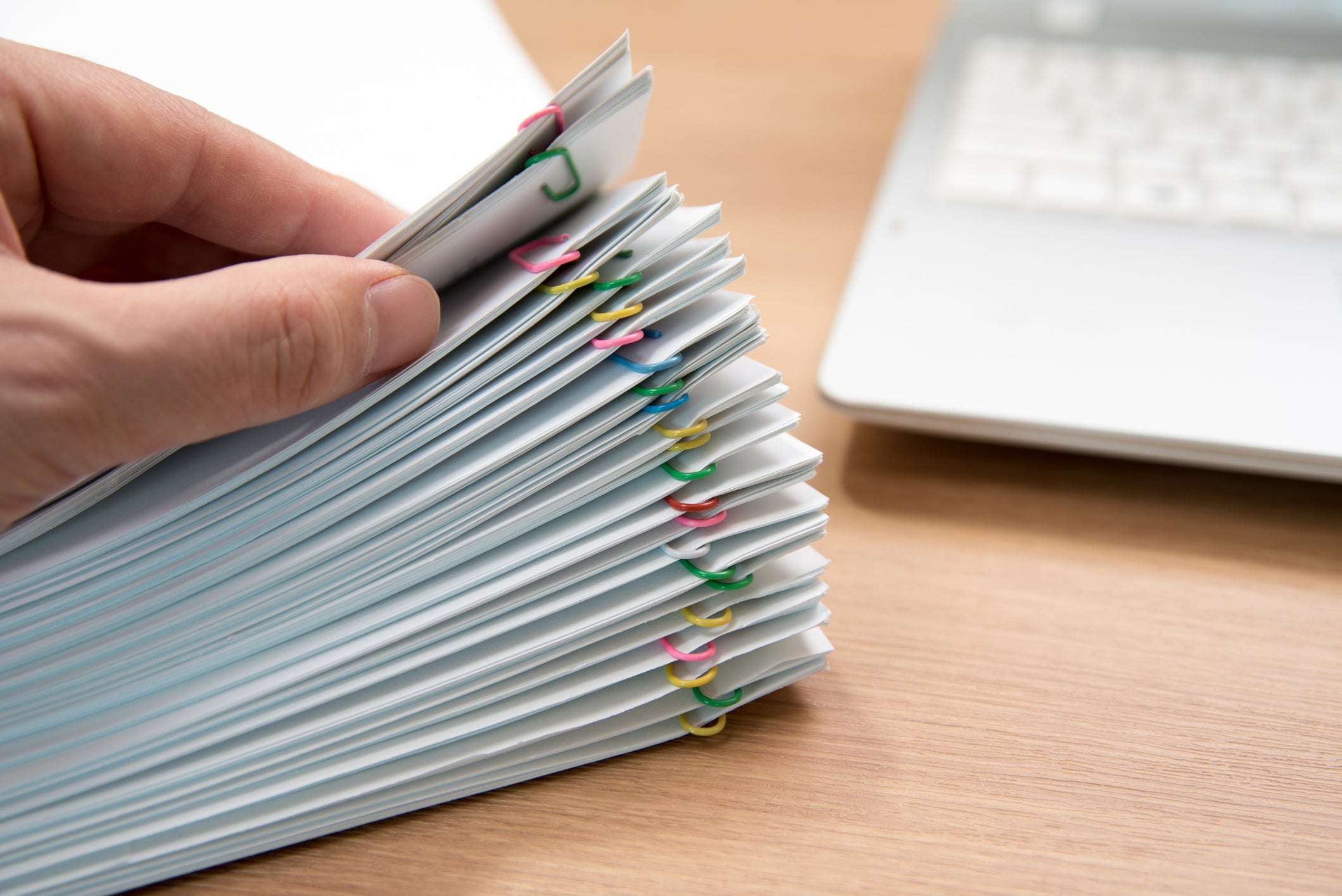 A person thumbs through several bundles of papers held together with paper clips.