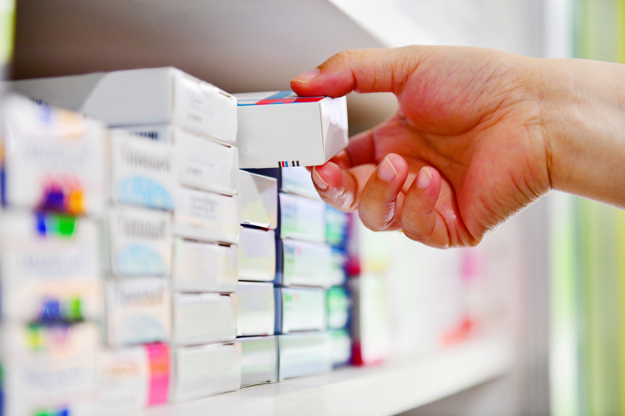 A hand grabs a medication box in a store.