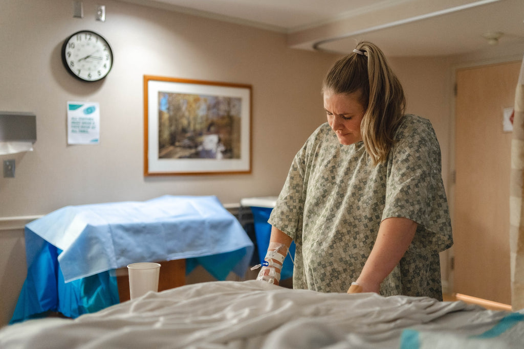A woman stands in a hospital gown, in a hospital room as she prepares to give birth.