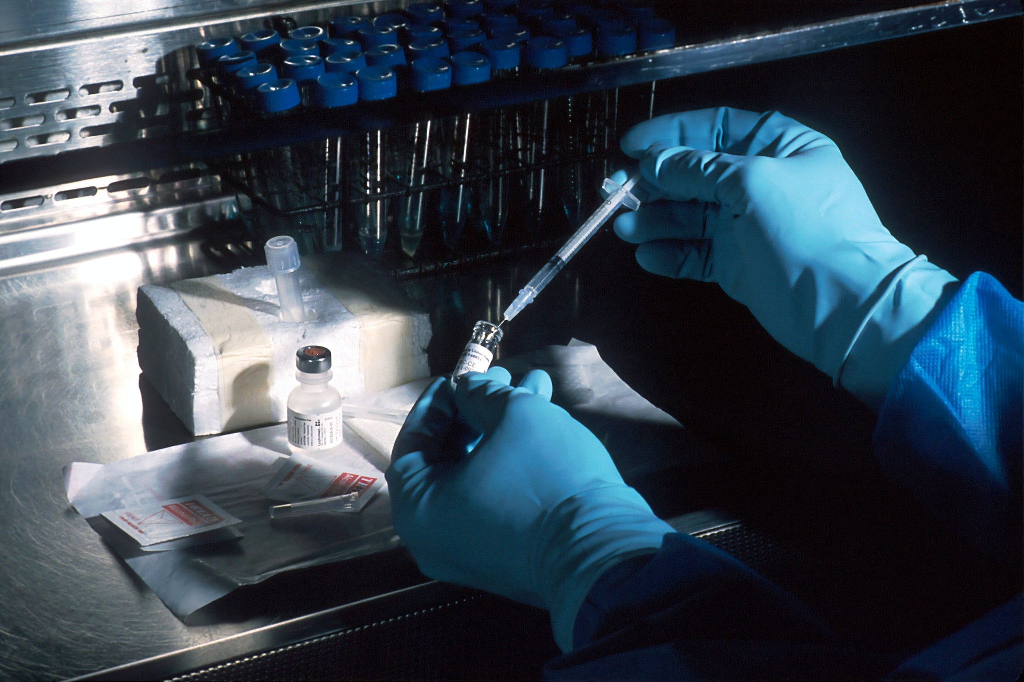 A lab technician uses a syringe to extract fluid from a test tube.
