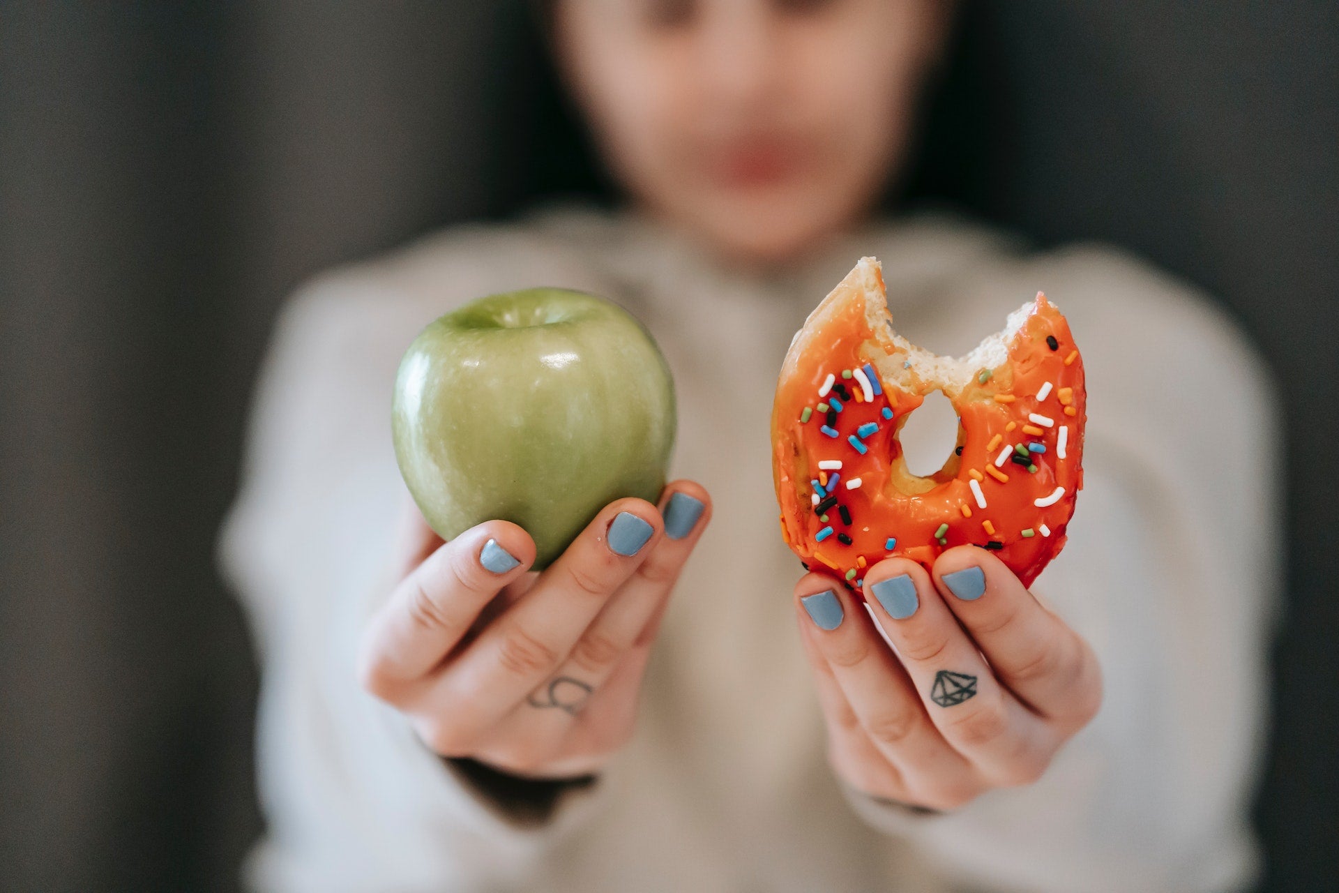 A woman holds up an apple in one hand and a donut in the other.