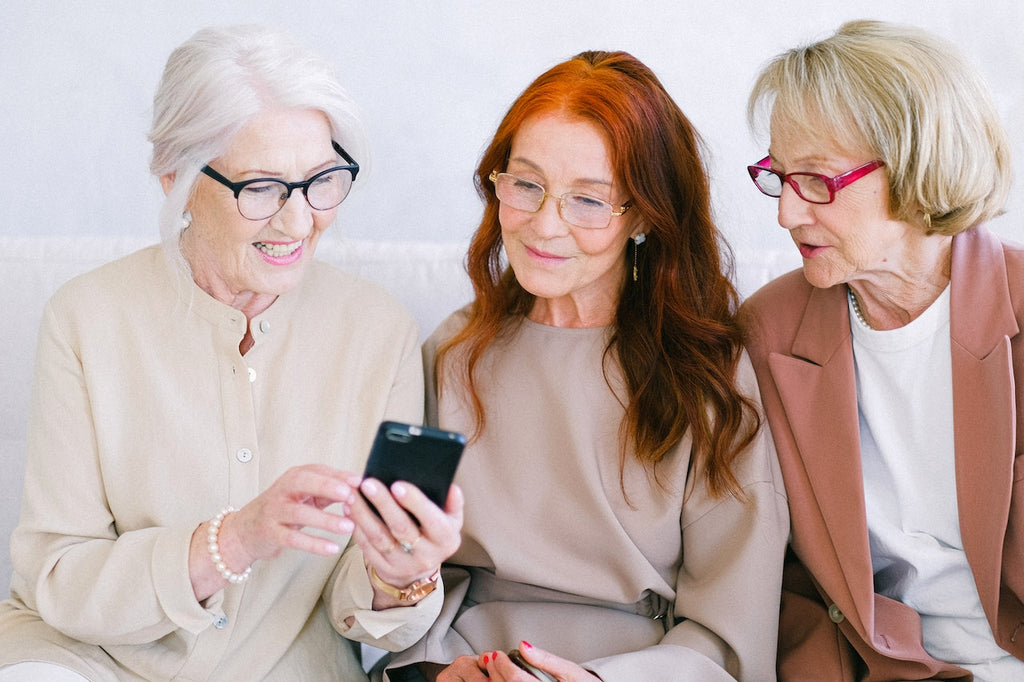 Three women sit together and smile while discussing something on a smartphone.
