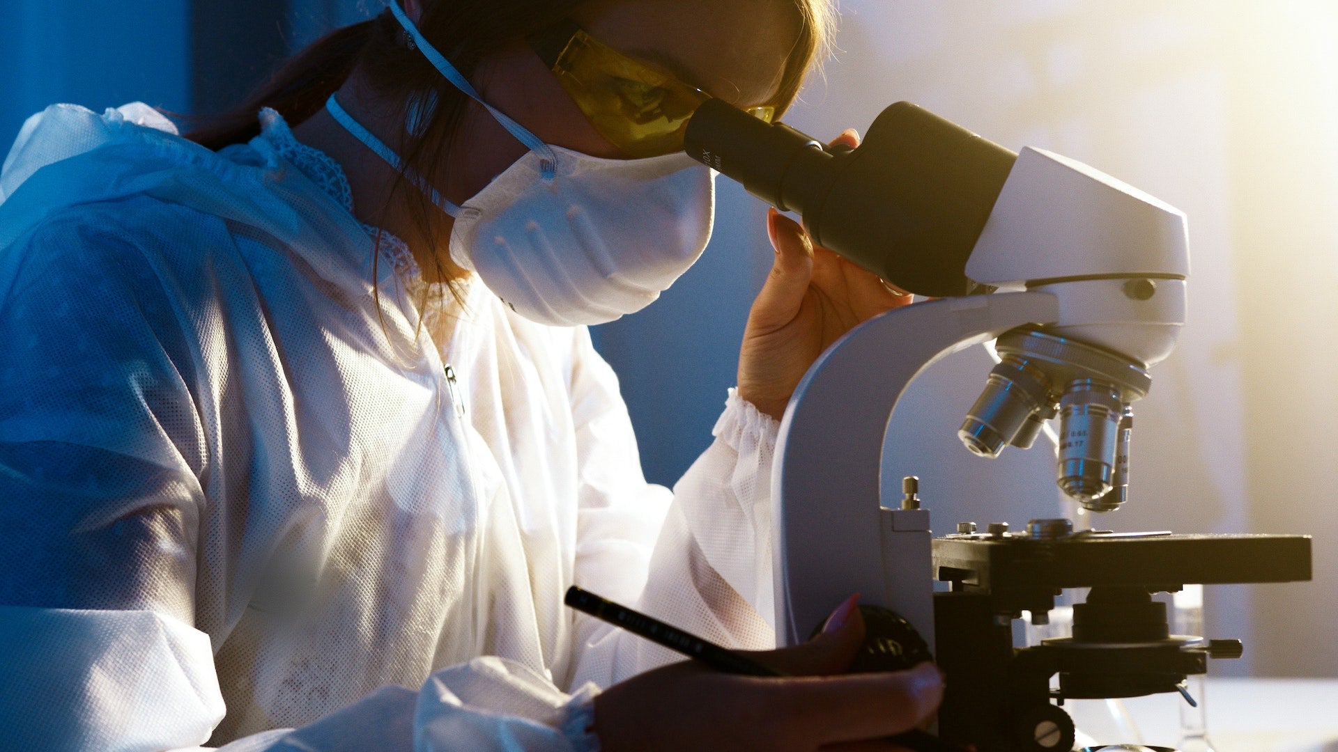 A lab technician examines a specimen under a microscope.
