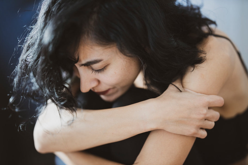 A woman hugs her knees to her chest and looks down.