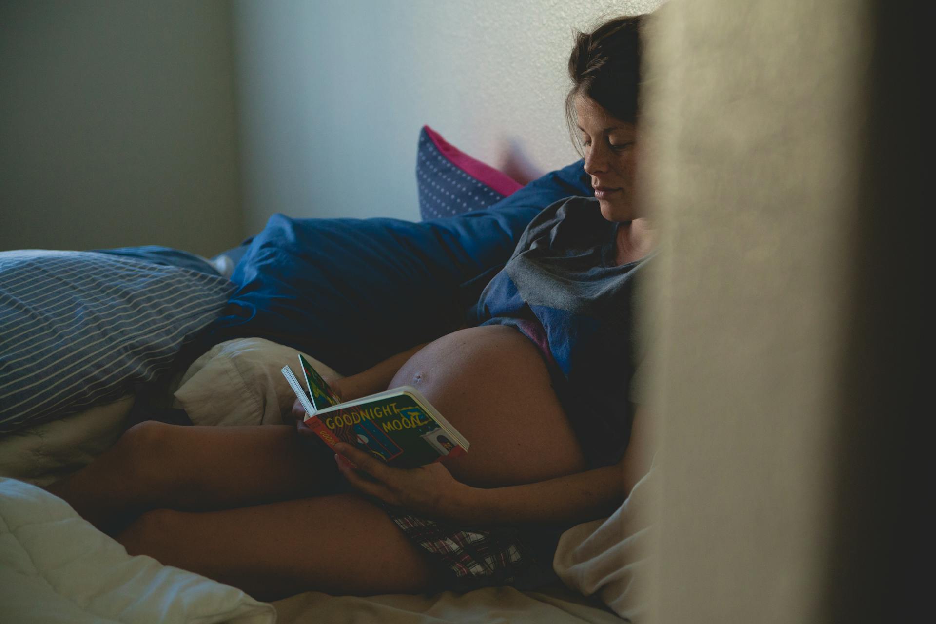 A pregnant woman reads on a bed.