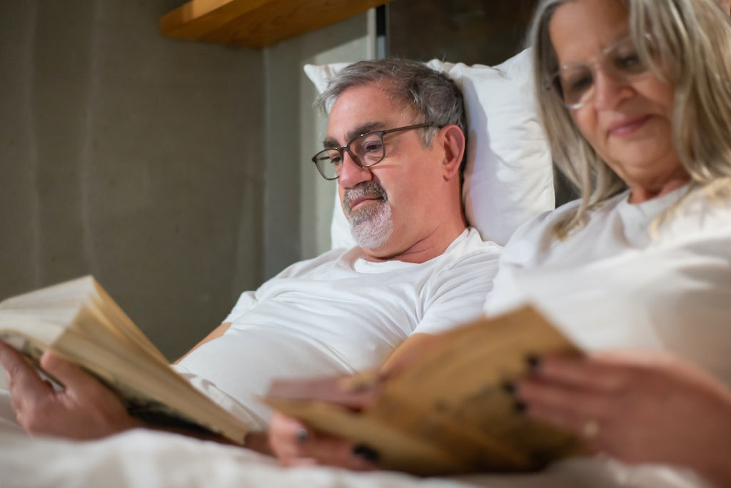 A couple relaxes in bed reading books.