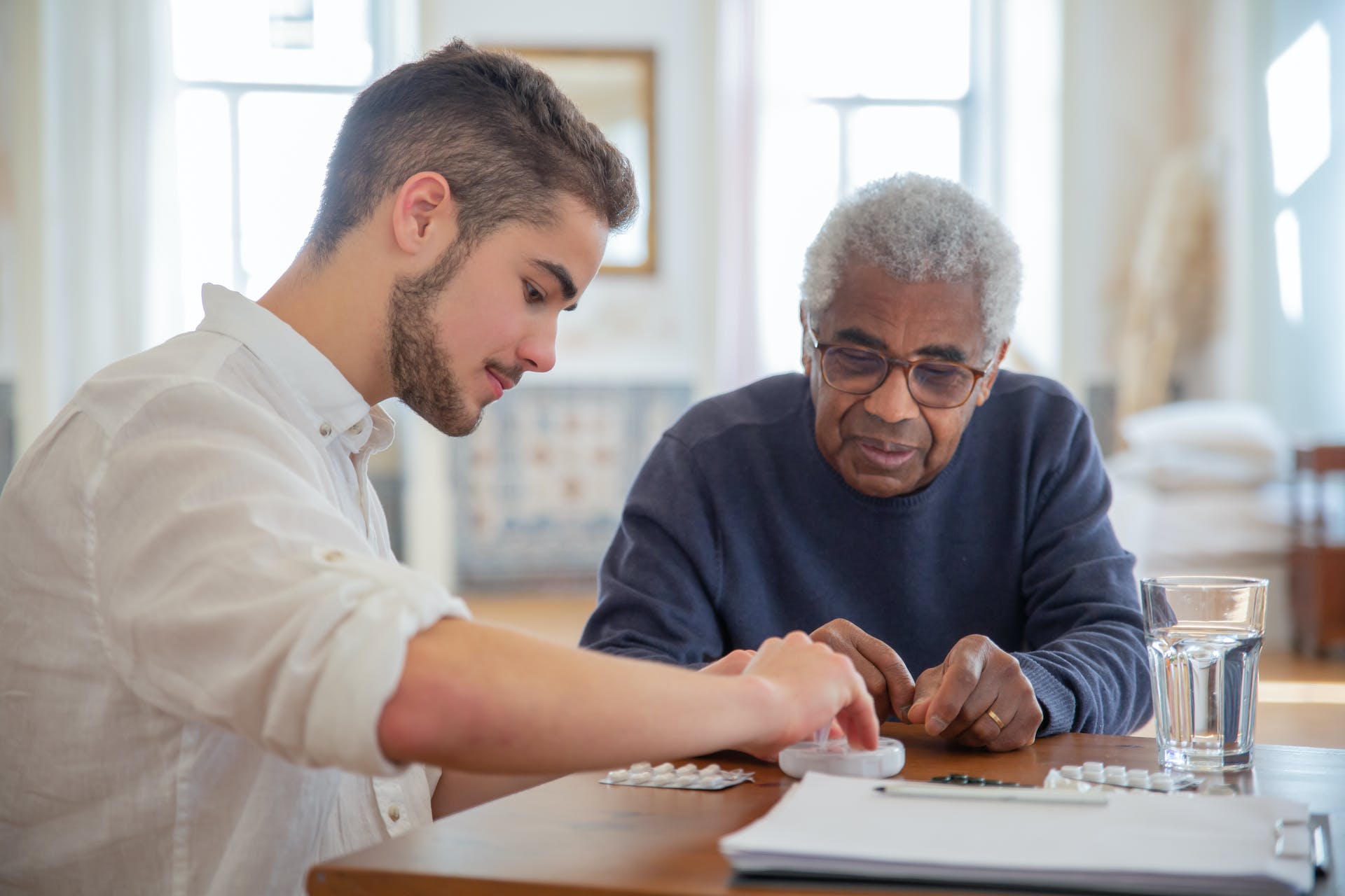 A young man helps an elderly man organize his medications.
