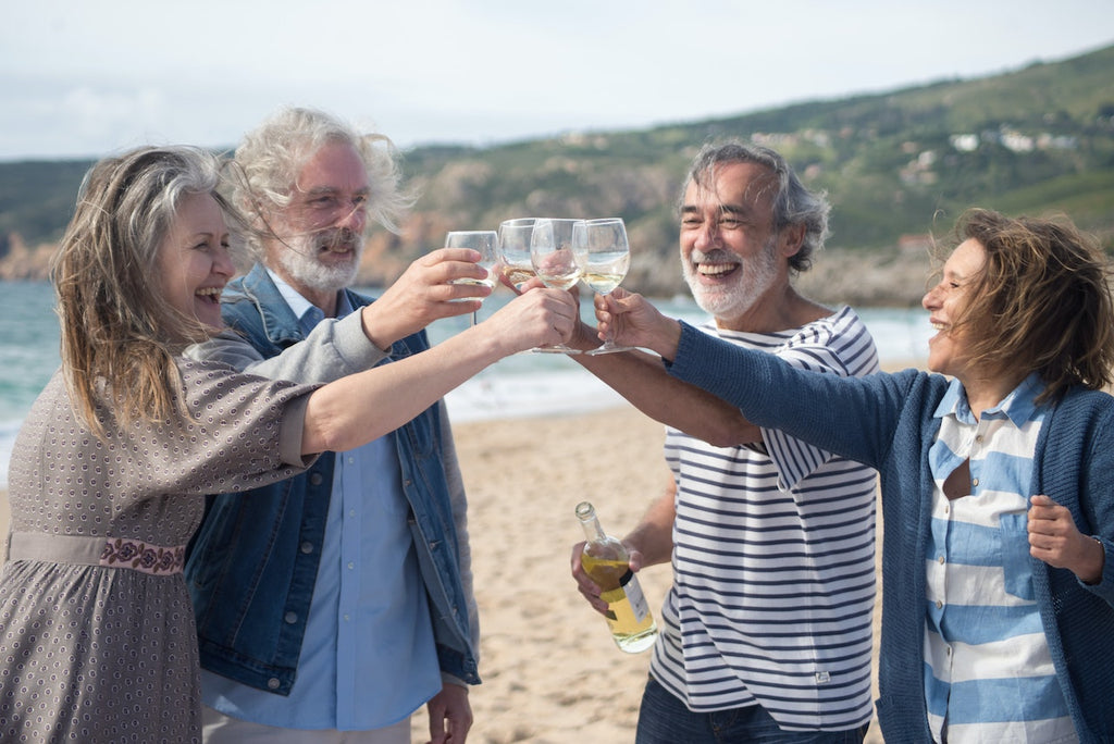 Four people stand on a beach with glasses of wine celebrating.