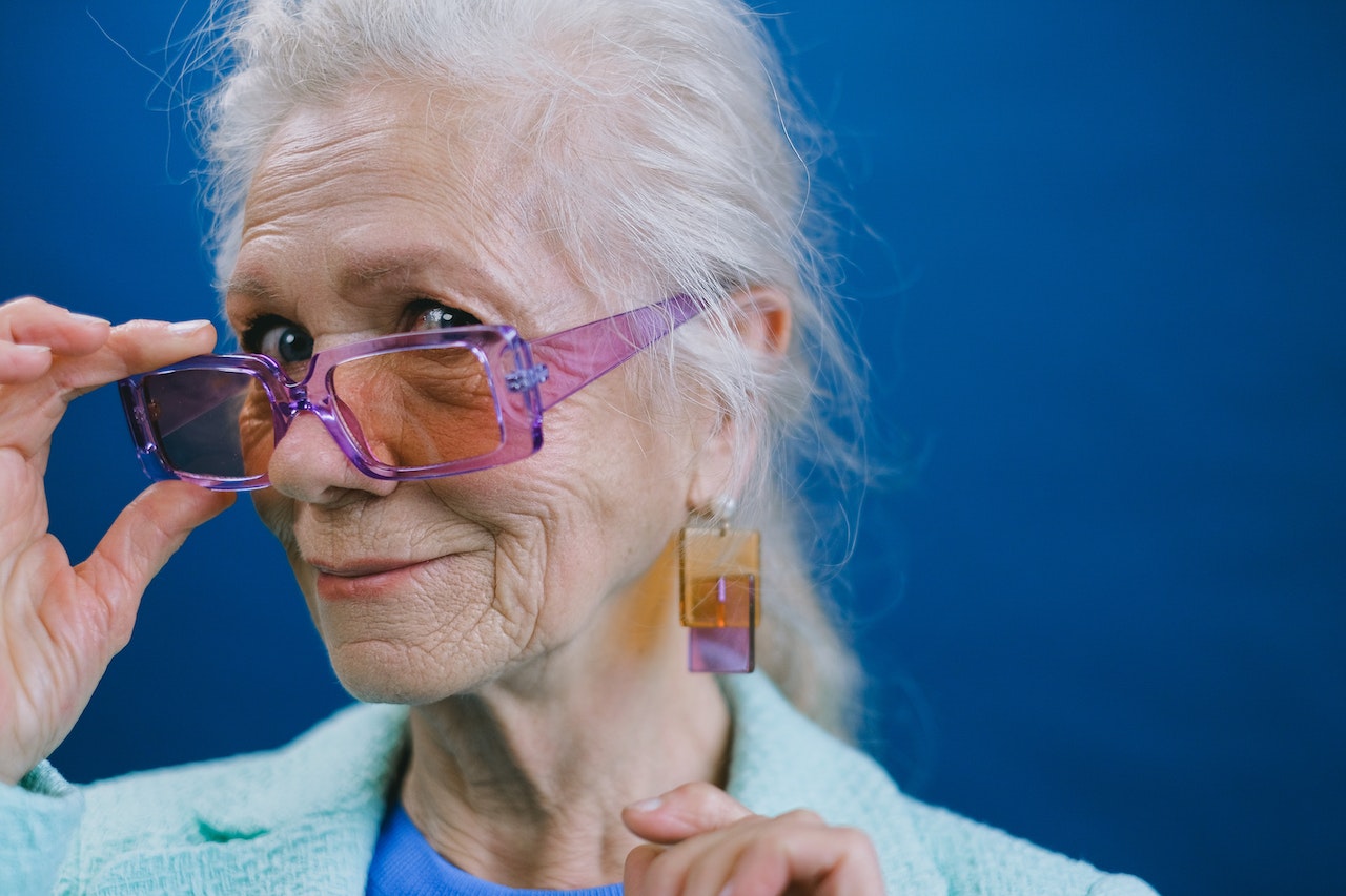 A woman with colored glasses looks at the camera and smiles.