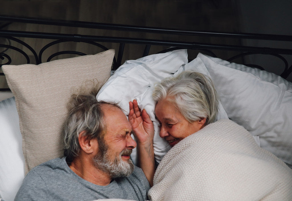 A man and a woman smile at each other in bed.