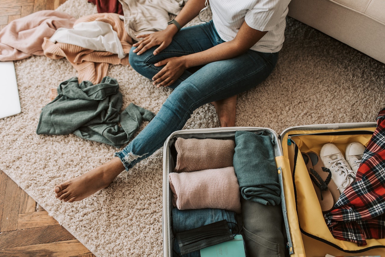 A woman sits on the carpet while she packs a suitcase.
