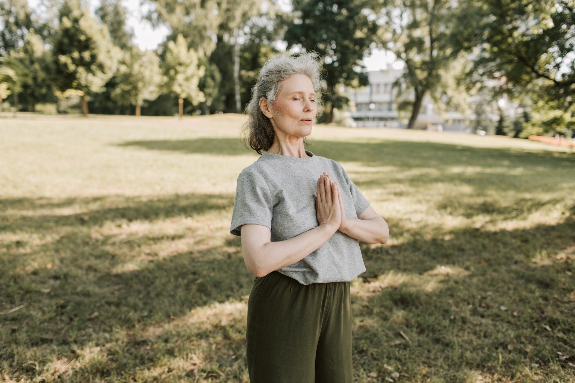 A woman in a park stands in a yoga pose.