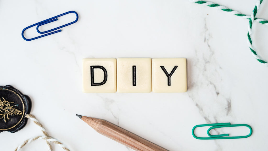 Scrabble tiles spelling out "DIY" are laid out surrounded by bits and pieces of desk drawer items.