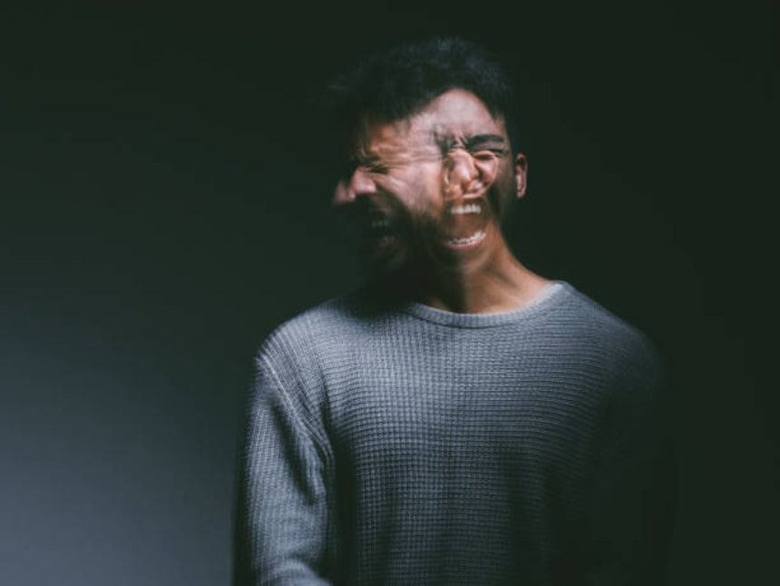 Studio shot of a young man experiencing mental anguish and screaming against a black background