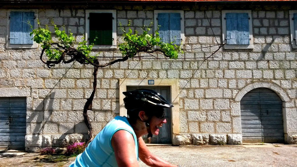Female cyclist smiling as she rides past a vine growing up a wall in Croatia