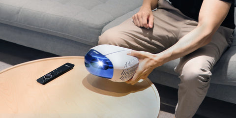 L500 Portable Triple Laser Projector held by a man in a cozy living room